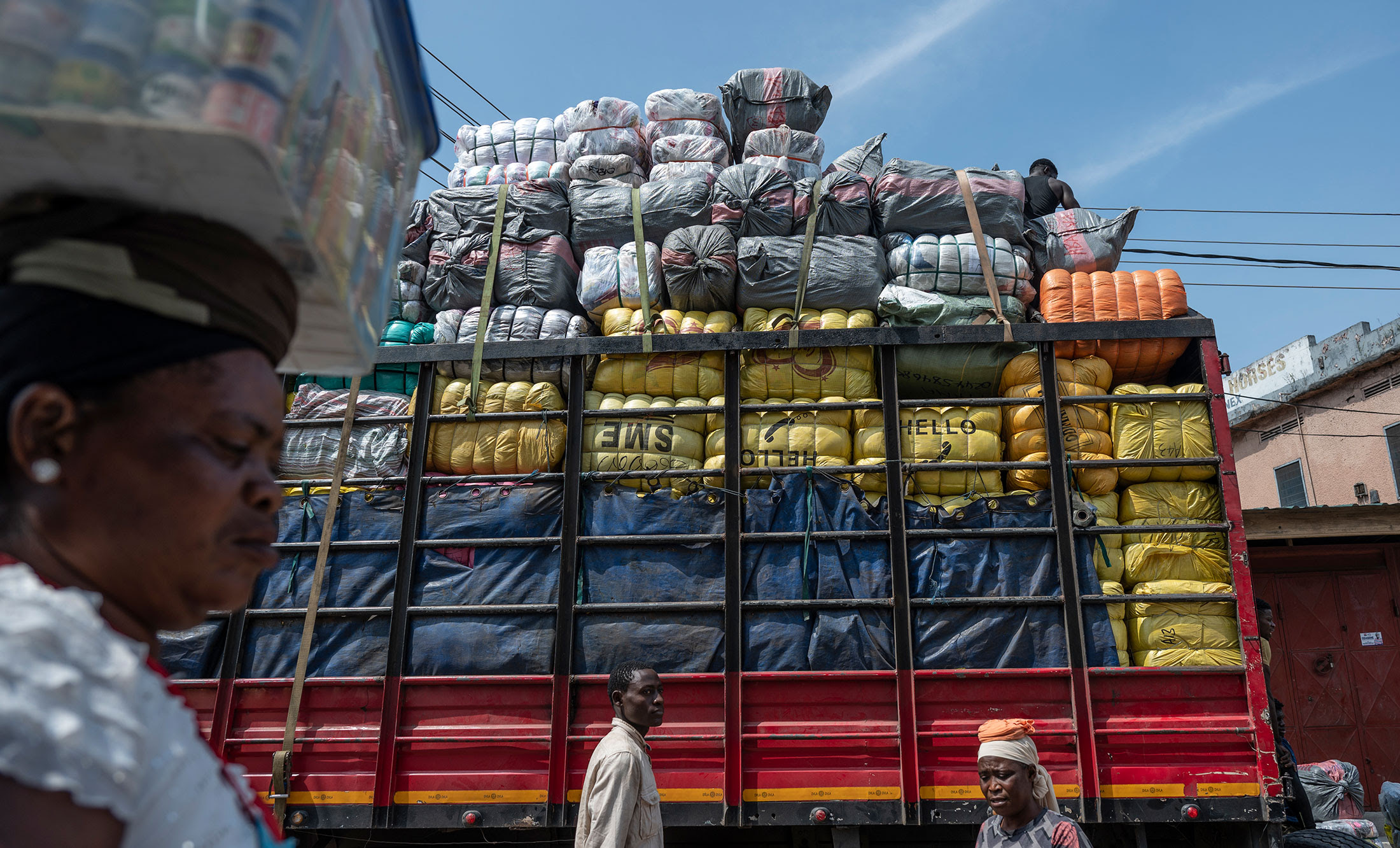 A Kayayei walks past a truck loaded with bales of secondhand clothing.