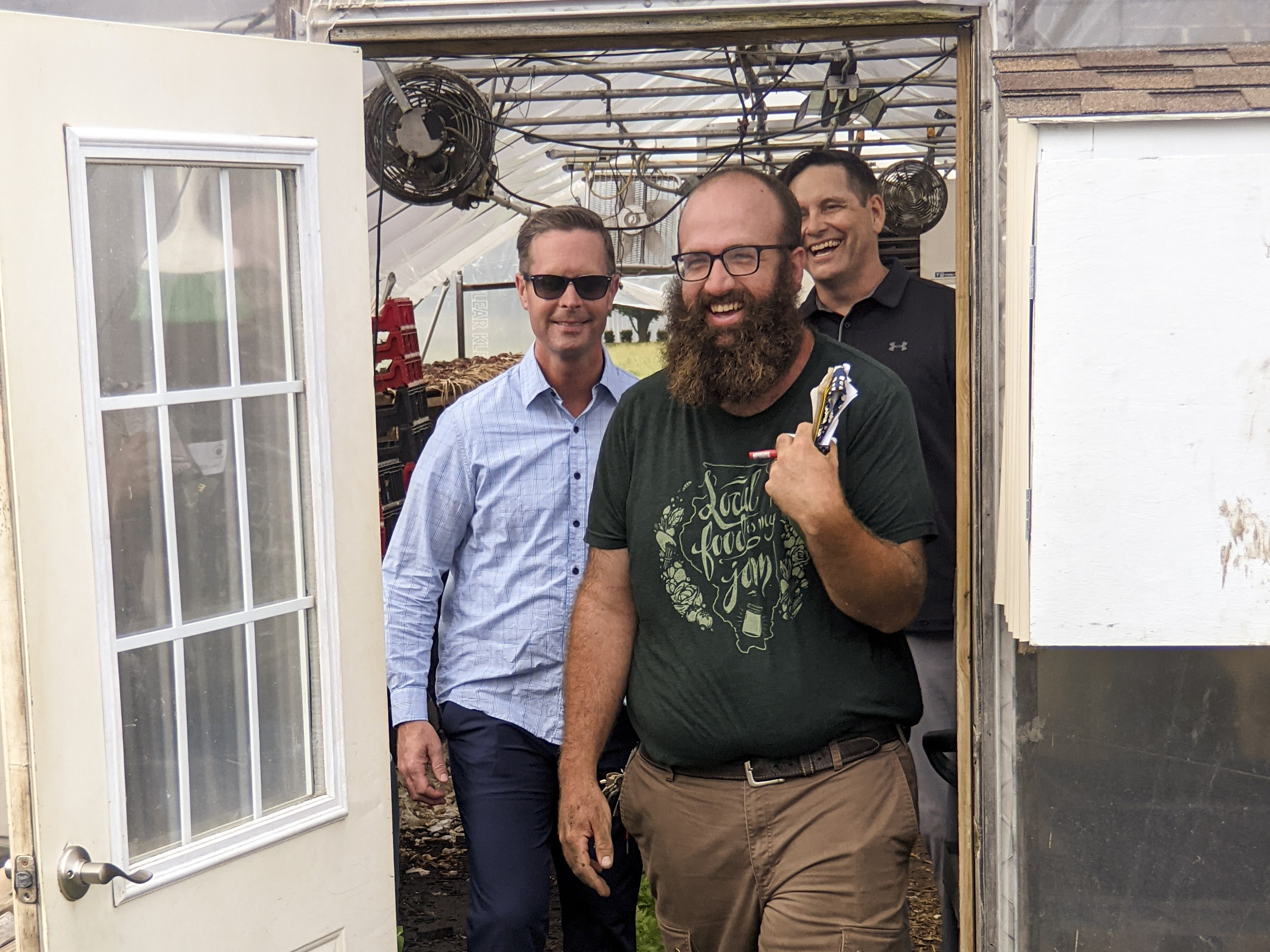 Congressman Rep. Rodney Davis, State Rep. Tim Butler and John Williams, farm manager of Sola Gratia exit a green house smiling and laughing.