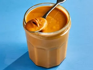 peanut butter in a jar with peanut butter in spoon resting on top