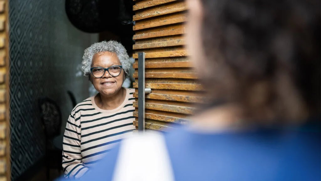 older woman peering from behind a door