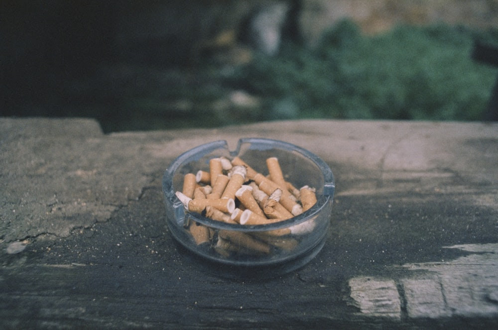 un bol en verre rempli de cigarettes posé sur une table en bois