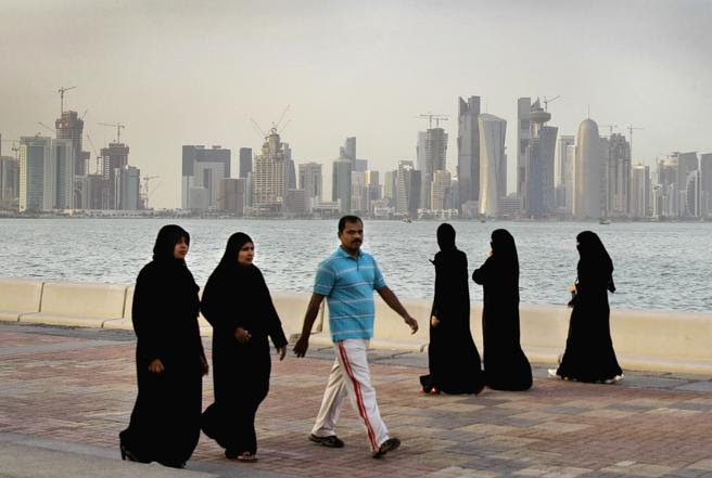 Mujeres cataríes y un hombre pasean junto al mar frente al skyline de Doha
