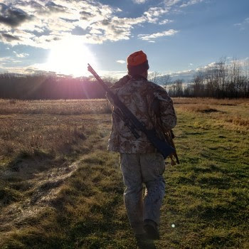 Hunter walking across plain while sun shines brightly