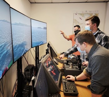 Photo of two people on a marine navigation simulator with another behind instructing 