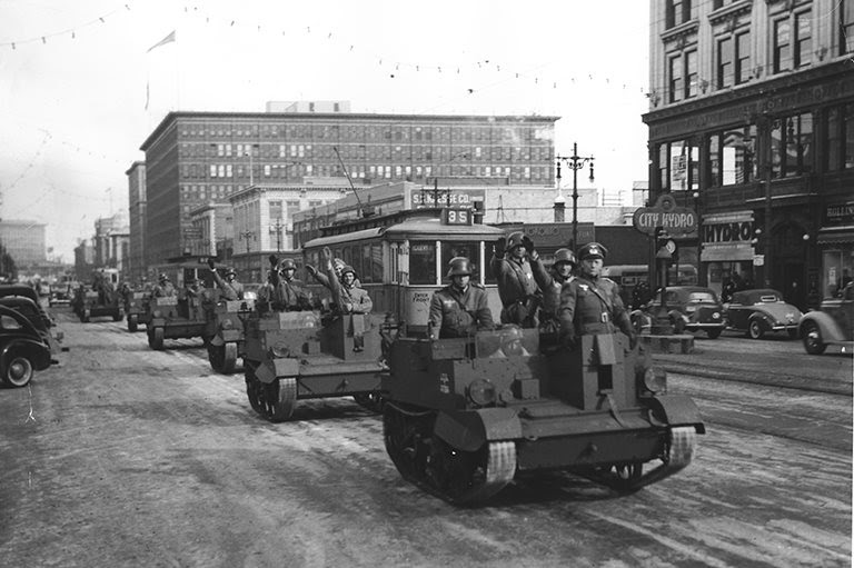 Black and white photo of tanks rolling through a downtown street.