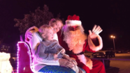 Santa with woman and child in a sleigh, smiling and waving.