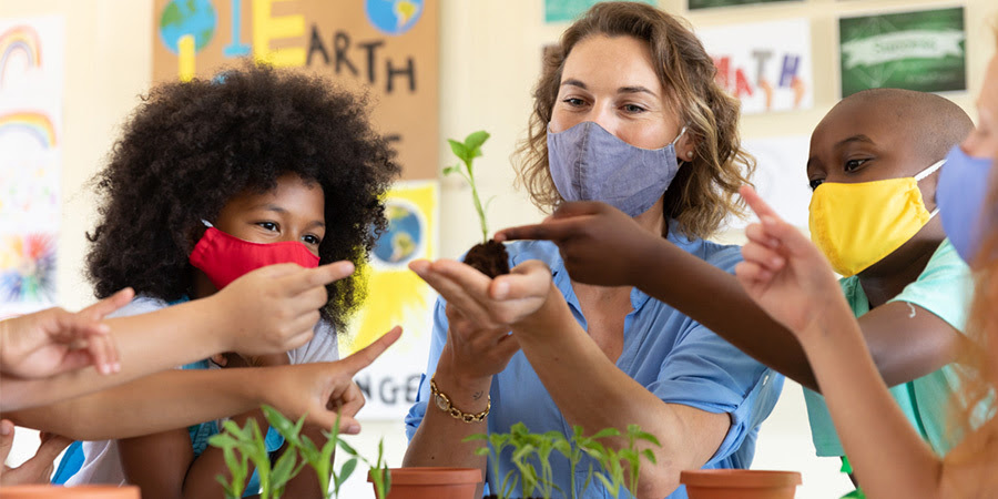 Imagen de un maestro y estudiantes con mascarillas y que miran los plantines