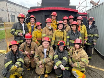 Sixteen people posing for a photo in firefighter gear