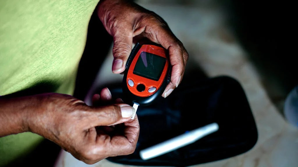 A person with type 2 diabetes using a red and black blood glucose meter.-2