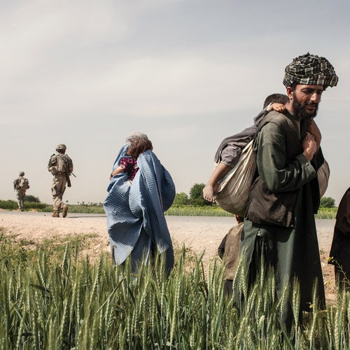 An Afghan man and an Afghan woman carrying children, with American troops in the background.
