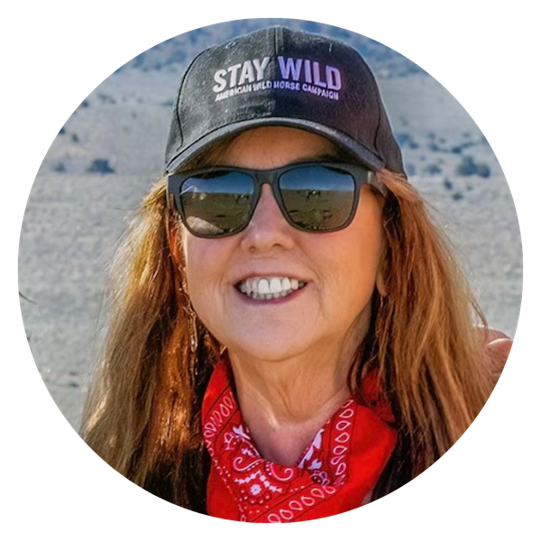Suzanne, a white woman with brown hair stands wearing sunglasses and a "stay wild" hat