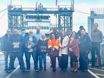 Several people posing for a photo at a ferry terminal with some holding up awards and certificates