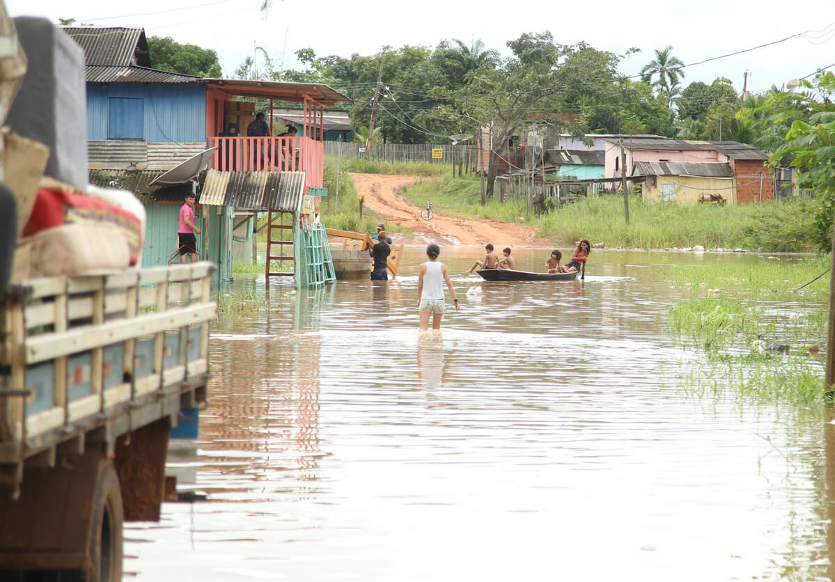 Moradores do Acre andam em meio a enchente, graças à cheia do Rio Acre. Na foto é possível ver crianças em um barco e outros moradores com água nos joelhos. Acre tem plano para lidar com as mudanças climáticas, mas não o executou