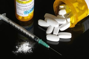Image: white pills spilled out of a pill jar, a needle, and a crushed pill. 