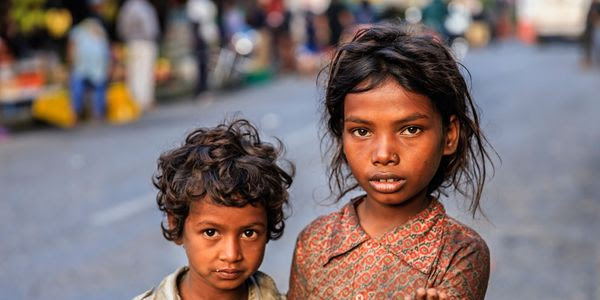 Two brown children in the street that appear to be dirty