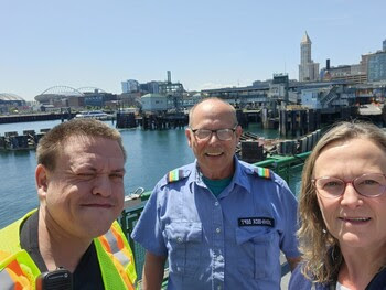 Three people posing for a selfie on the outdoor deck of a ferry with Seattle skyline in the background