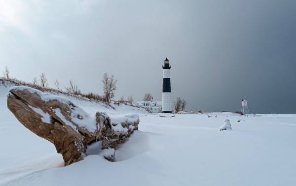 A gray winter storm blows across a frozen lake, bufetting a solitary lighthouse.