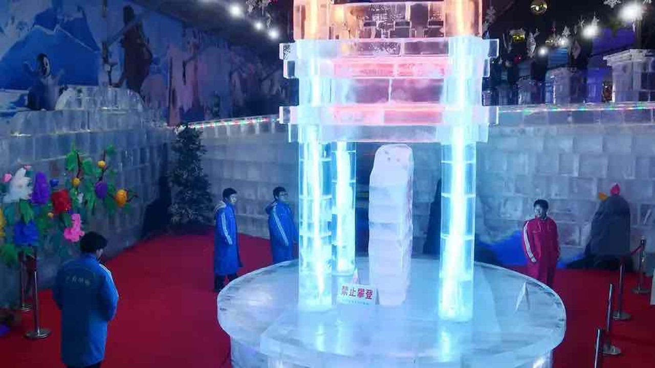 People admire ice pillars lit from within by bright blue and pink lights. 