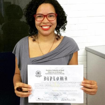Raíssa é ex-estudante do prouni. Ela é uma mulher negra com cabelo escuro e cacheado na altura da nuca. Ela veste blusa cinza, batom e óculos de grau vermelhos. Larissa está segurando o diploma com as duas mãos