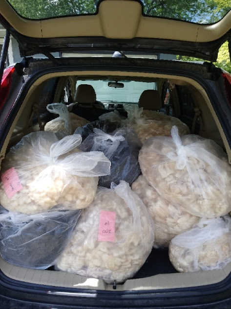 The tailgate of an SUV is open, showing a vehicle full of bags of wool in cream, brown and black