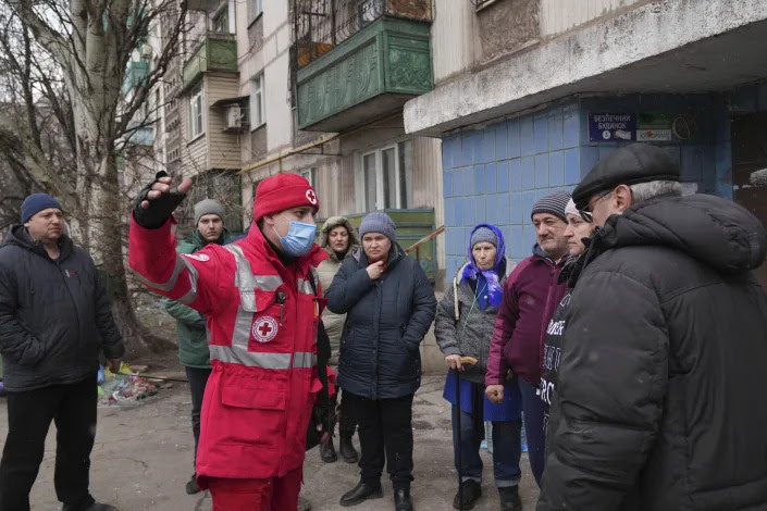 People talk with a Red Cross worker next to an apartment building in Mariupol. 