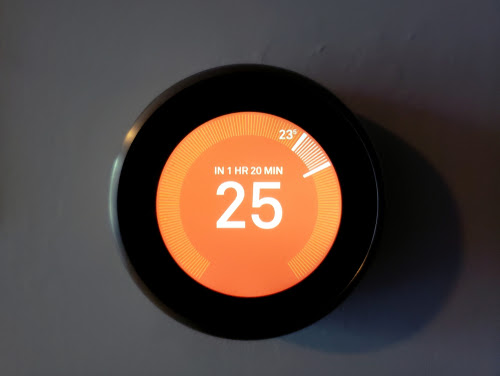 The temperature on modern circle thermostat on heat will reach to 25 Celsius in 1hr 20mins from 23.5 Celsius_ Programmable Thermostat - Wireless Learning_ Soft focus in dark blurred background