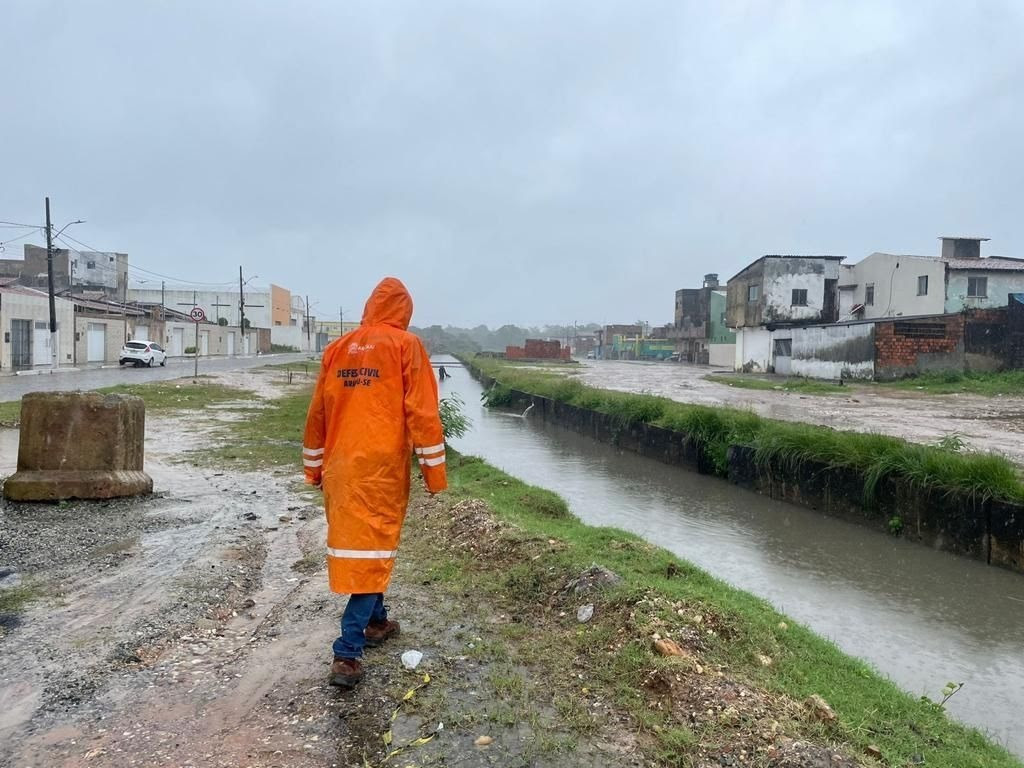 Funcionário da Defesa Civil de Aracaju andando em frente a um córrego com alta vazão, graças às chuvas intensas. Aracaju não tem plano para lidar com os efeitos das mudanças climáticas