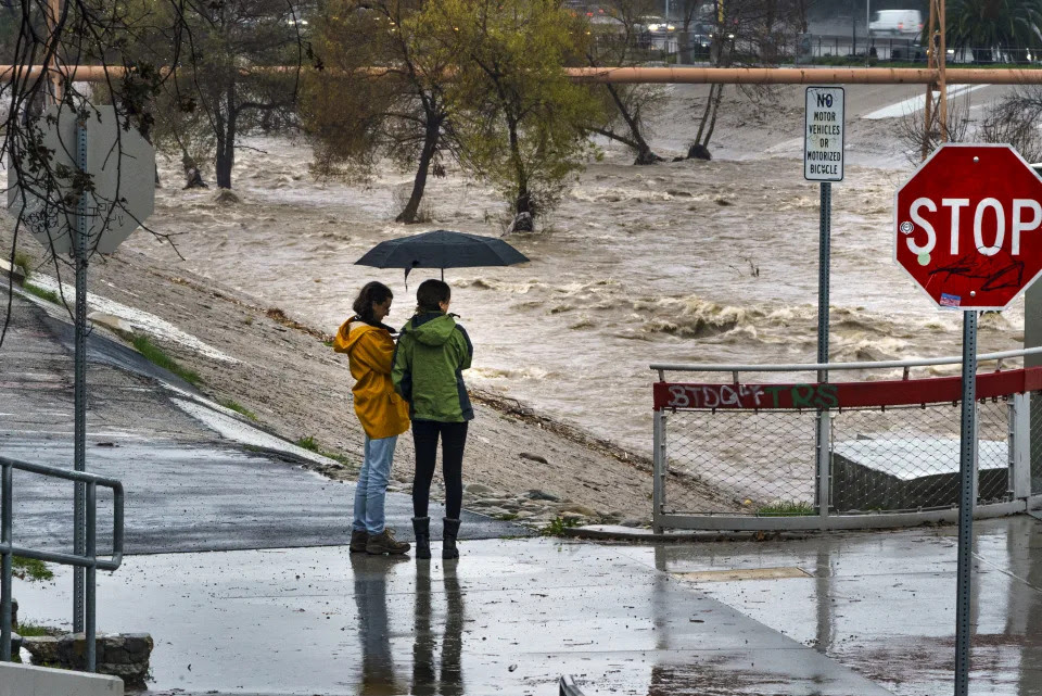 People watch the high volume of storm rain water flowing downstream at the Los Angeles River in Los Angeles on Saturday, Jan. 14, 2023. Storm-battered California got more wind, rain and snow on Saturday, raising flooding concerns, causing power outages and making travel dangerous. (AP Photo/Damian Dovarganes)