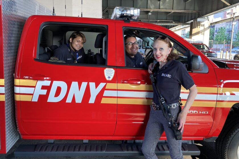 Two members of New York City's Behavioral Health Emergency Assistance Response Division (B-HEARD) in a New York City Fire Department vehicle, with a third member standing in front of it, all smiling at the camera.