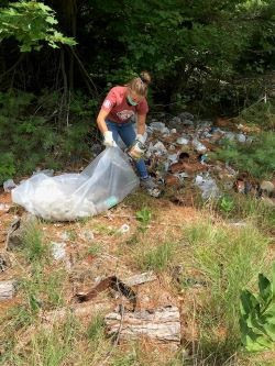 A young person cleans up trash in a forest