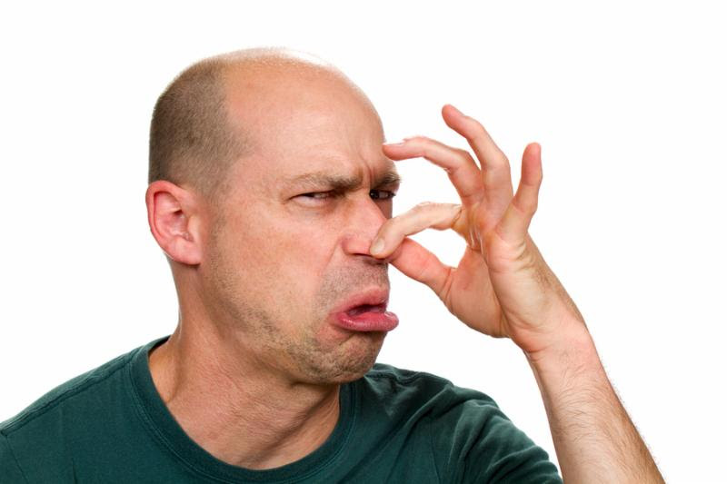 Man smells something stinky and pinches his nose to stop the bad odor.