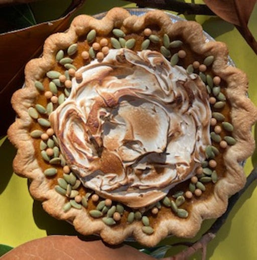 Toasty brown pie shell with ochre colored pumpkin pie filling and a generous dollop of toasted meringue. Decorated with toasted pepitas and tiny milk chocolate pearls. On a lime green background.