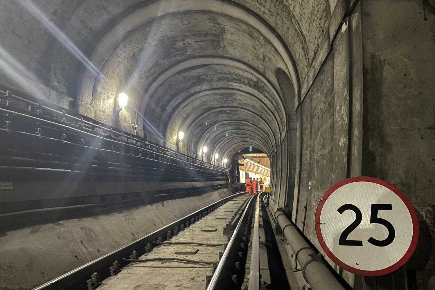 Arched single track railway tunnel with 25 mph sign and group of workers wearing orange high vis