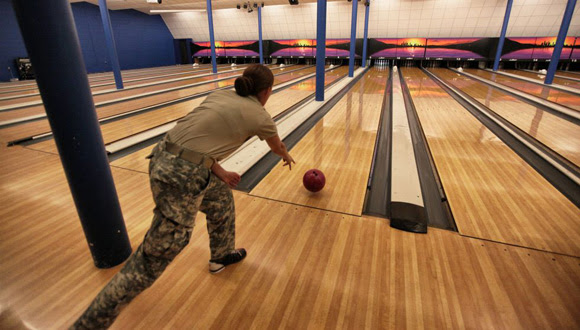 Una soldado juega en la bolera en la base naval de Guantánamo. Algunas personas llevan bolsas de diseño militar para transportar sus bolos. La bolera está al lado de un gimnasio y de un campo de fútbol americano.