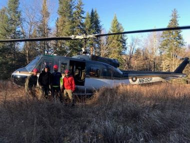 Rangers and helicopter in field near woods during mission