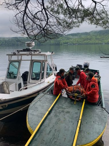 Rangers loading injured hiker on to small boat on the water