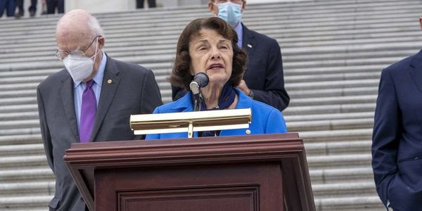 The late Senator Dianne Feinstein stands in front of a podium.