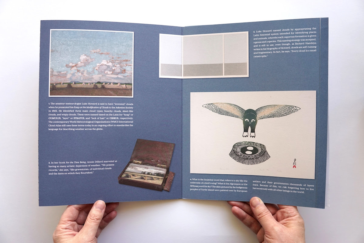 Two hands hold open a double-page spread of Cloud Collection showing images of artworks and texts.