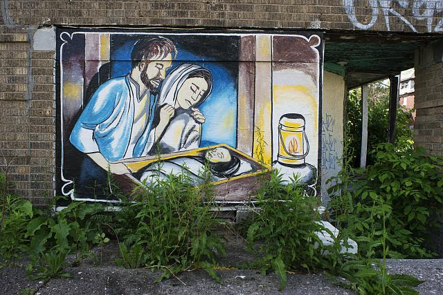 McClellan at Goethe, Detroit, 2014. Nativity scene painted on the ruins of an apartment building. Berry, the postman, said, "The neighborhood is being blessed, the area is so bad that they could use a blessing." Kat, the lady that lives across the street hired a sign painter. The Goethe Building erected in 1924, is according to the postman "Not so much the eyesore that used to be" explaining that "The murals on it are about faith"