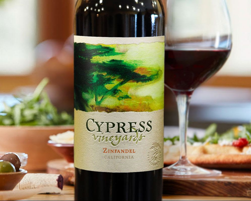 Bottle and glass of Cypress Vineyards Zinfandel on a table next to inviting food.