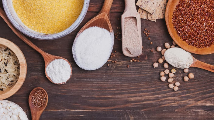 An image displays a variety of gluten-free flours in different bowls and spoons on a wooden background.