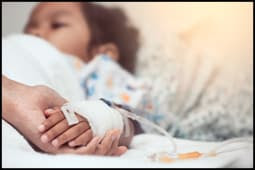 The figure above is a photograph of a small child lying in a hospital bed holding an adult’s hand.