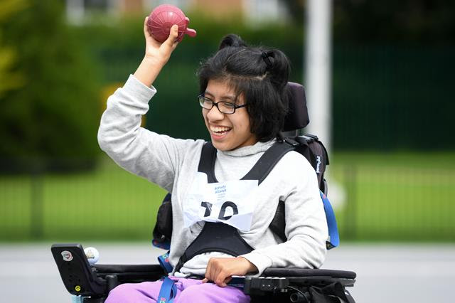 A girl in her powerchair throwing a weighted ball on an athletics field