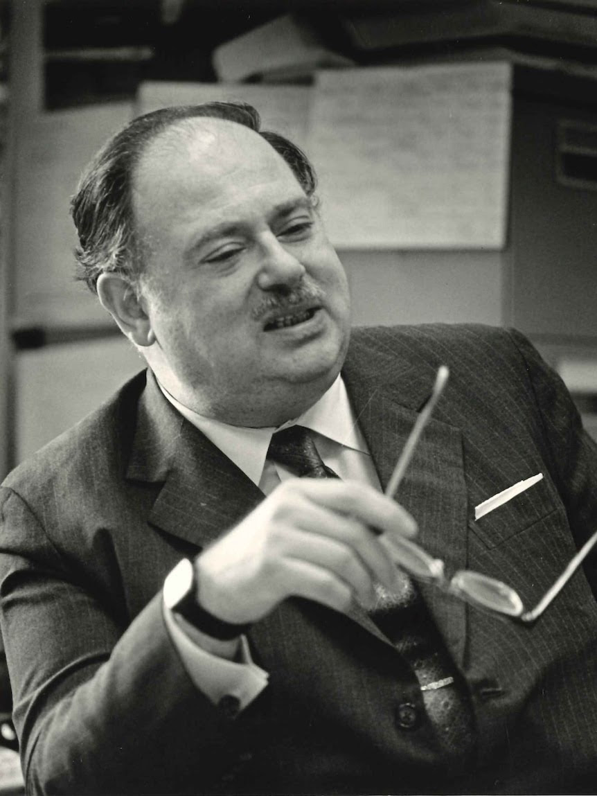 Portrait of an older man who gestures with his glasses 