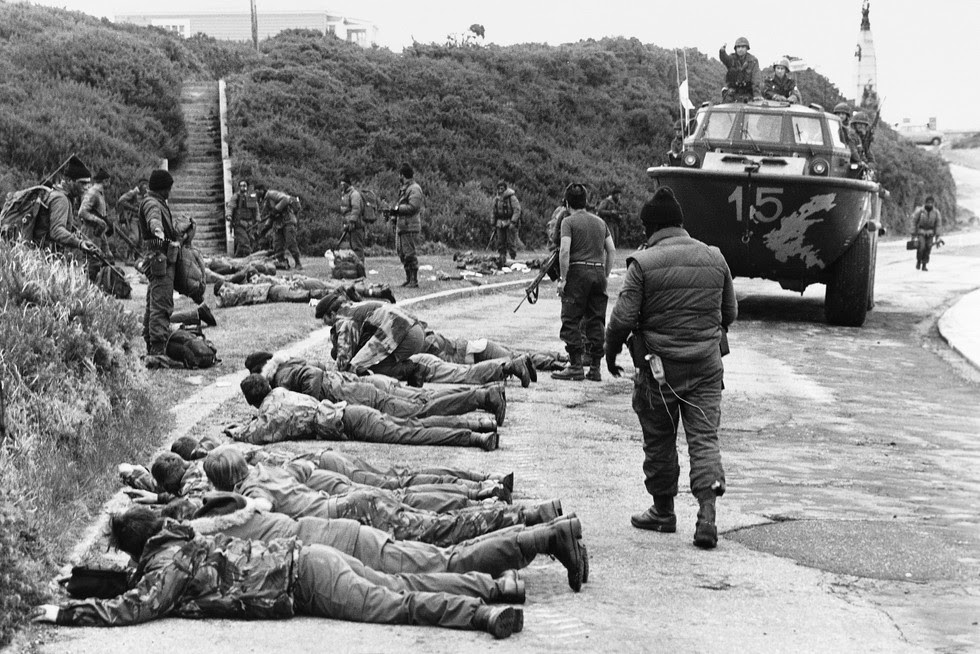 British soldiers lie on the floor an gumpoint during the Falklands War, guarded by Argentine soldiers