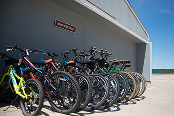 row of rental bicycles next to building with lake in background