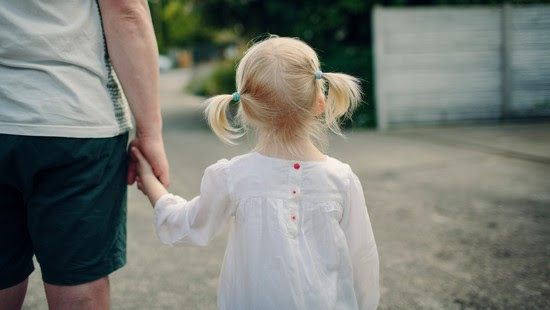 A little girl with pigtails holds an adult's hand.
