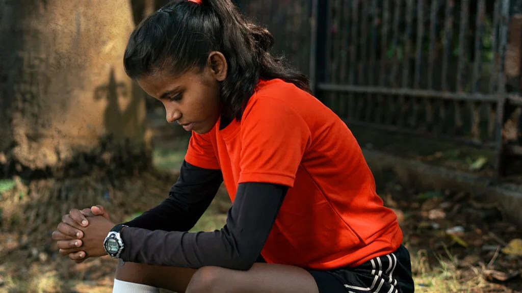 Girl in. soccer kit resting arms on knees wondering how to relieve menstrual cramps or period pain.