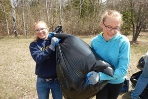 Two young women moving a black garbage bag, after cleaning up a dump site in a Michigan forest 