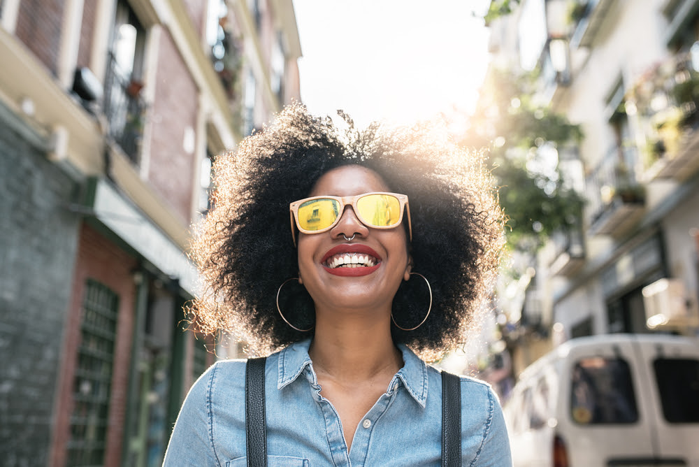 black woman on a city street smiling wearing sunglasses